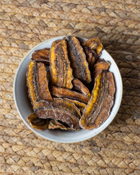 Eine Schale mit getrockneten Bananenscheiben auf einem geflochtenen Untergrund.