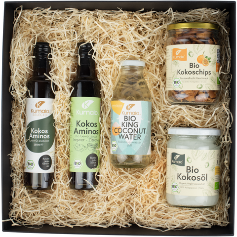 Geschenkbox mit Bio Kokos-Produkten, darunter Kokoswasser, Kokosöl, Kokoschips und zwei Flaschen Kokos-Aminos.