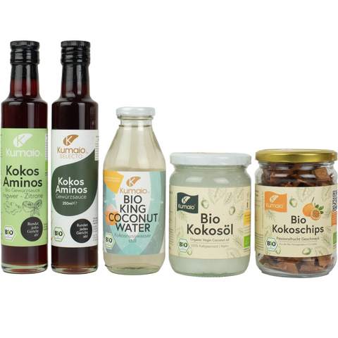 Fünf Bio-Produkte von Kumaio, darunter Kokos-Aminos, Kokoswasser, Kokosöl und Kokoschips, nebeneinander aufgestellt.