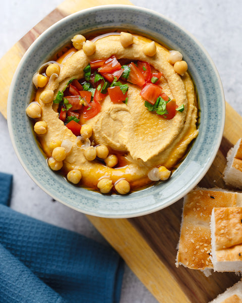 Schale mit cremigem Hummus, garniert mit Kichererbsen, Tomatenwürfeln und Petersilie, serviert mit Fladenbrot und verfeinert mit Kumaio Bio Aminos.