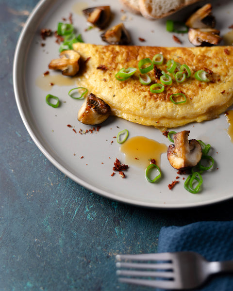 Goldgelbes Omelett mit gebratenen Champignons und frischen Frühlingszwiebeln, serviert auf Teller mit Brot und Sauce, verfeinert mit Kumaio Bio Aminos Soße.
