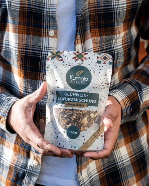 Person in kariertem Hemd hält eine Packung Kumaio Glühwein-Gewürzmischung in den Händen.