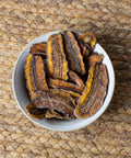 Eine Schale mit getrockneten Bananenscheiben auf einem geflochtenen Untergrund.