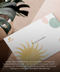 Alt-Text: Eine handgeschriebene Karte mit einem Sonnensymbol und dem Spruch „Be your own sunshine“ liegt auf einem Tisch. Daneben eine grüne Pflanze im Hintergrund. Text im Bild erklärt, dass Geschenke durch eine personalisierte Nachricht auf der Karte ergänzt werden können.