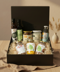Große Geschenkbox mit Kumaio Bio Kokos Aminos, Bio Kokoschips Natur, Bio Kokosöl, Bio King Coconut Water sowie Bio Bananenblüten, Bio Sweet Jackfruit und Bio Jackfruit Natur, dekorativ arrangiert in schwarzer Box mit Holzwolle.