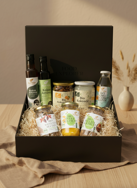 Große Geschenkbox mit Kumaio Bio Kokos Aminos, Bio Kokoschips Natur, Bio Kokosöl, Bio King Coconut Water sowie Bio Bananenblüten, Bio Sweet Jackfruit und Bio Jackfruit Natur, dekorativ arrangiert in schwarzer Box mit Holzwolle.