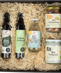 Geschenkbox mit Bio Kokos-Produkten, darunter Kokoswasser, Kokosöl, Kokoschips und zwei Flaschen Kokos-Aminos.