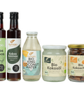 Fünf Bio-Produkte von Kumaio, darunter Kokos-Aminos, Kokoswasser, Kokosöl und Kokoschips, nebeneinander aufgestellt.