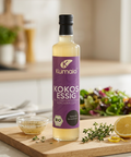 Kumaio Bio Kokosessig aus fermentiertem Kokoswasser auf einem Holzbrett mit Dressing, Kräutern, Zitrone und frischem Salat im Hintergrund.