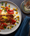 Ein Teller mit gebratenem Lachs auf Nudeln, garniert mit roten Paprikascheiben, gelben Paprikawürfeln und fein geschnittenem Ingwer.
