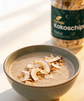 Bio Kokoschips natur von Kumaio im Glasgefäß als Topping auf cremigem Frühstücks Porridge mit Kokosraspeln