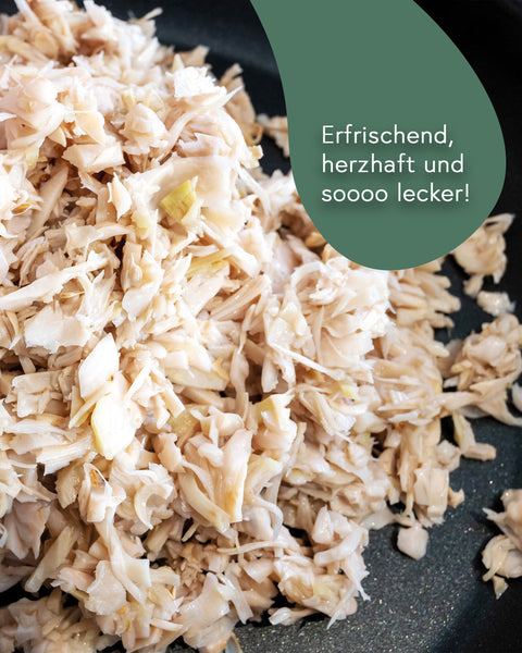 Nahaufnahme von zerkleinertem Jackfruit-Fruchtfleisch in einer Pfanne. In der Ecke ist ein grüner Kreis mit der Aufschrift: "Erfrischend, herzhaft und sooo lecker!