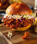 Pulled-Jackfruit-Burger mit BBQ-Sauce und cremigem Coleslaw in einem weichen Brioche-Brötchen, serviert auf einem Holzbrett.